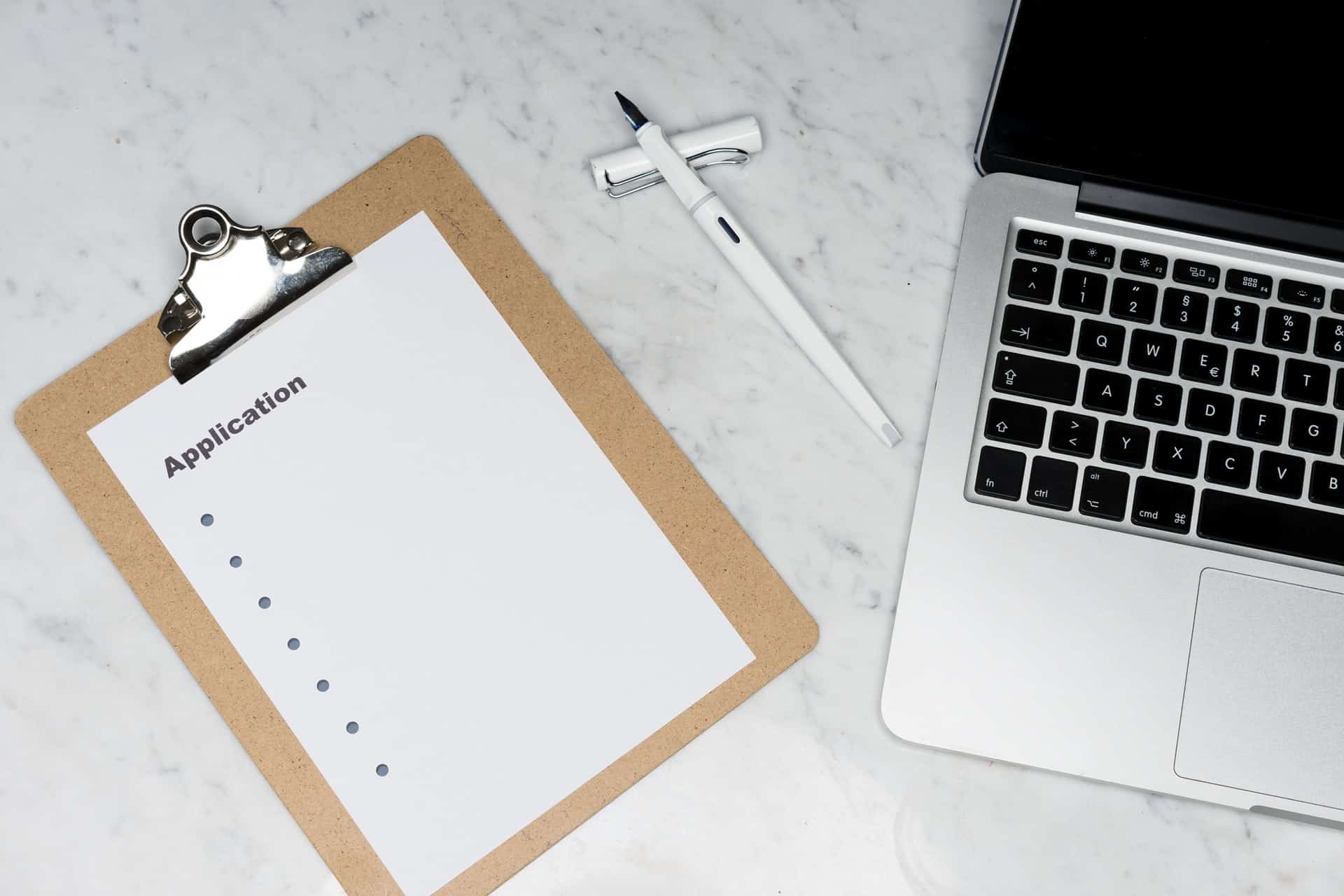 Laptop next to a clipboard which has an application form on it